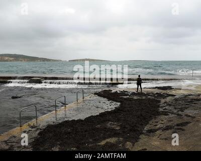 Man standing on waterfront looking out to sea, St Paul's Bay, Bugibba, Malta Stock Photo