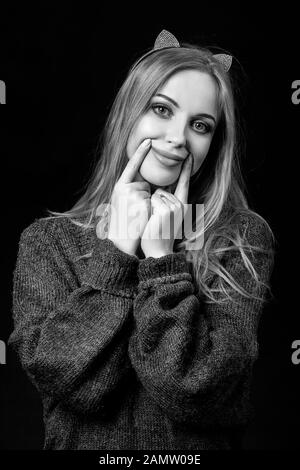 sad young woman show fake smile on dark background, monochrome Stock Photo