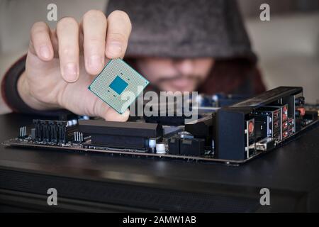 Concept for hacker in control of personal data from computer. Unrecognizable man wearing a hoodie while holding a computer chip between his fingers, a Stock Photo