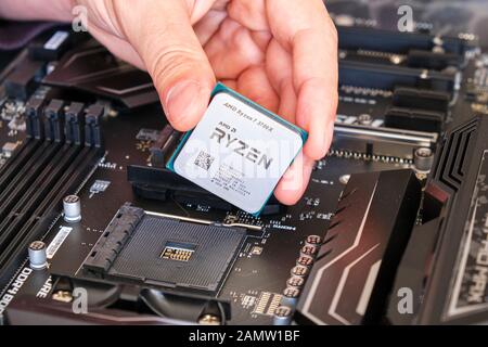 Los Angeles, CA, USA - December 30, 2019: AMD Ryzen 3700X CPU in technician fingers, above a motherboard, part of a custom PC build. Stock Photo
