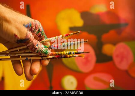 decorated painted artist paint brushes in colored hand.hand holding art brushes .orange and yellow background Stock Photo