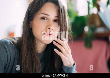 Portrait of smiling cute hipster girl staring on camera while writing college exercises in notebook. Stock Photo