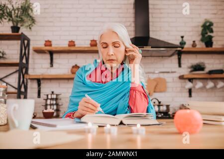Grey-haired beautiful elderly lady in blue shawl making notes Stock Photo