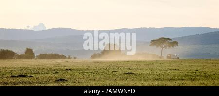 A safari vehicle sends up dust as it drives across a dry Maasai Mara, Kenya. Stock Photo