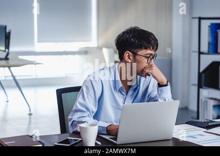 asian businessman get stress and thinking when working with laptop on desk at modern office.business fail concept.man rest hand on chin on table when Stock Photo