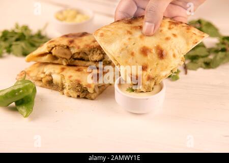 Hand dipping stuffed naan into sauce with green chillies on the side Stock Photo