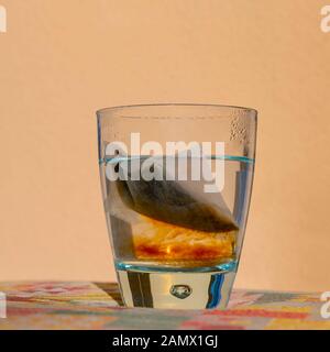 An infusion tea bag inside a transparent glass of hot water releases its precious content Stock Photo