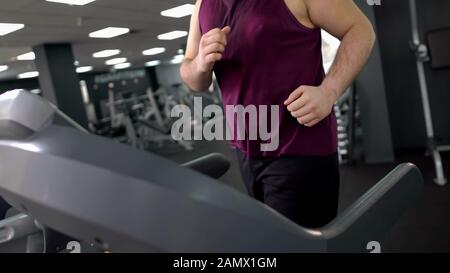 Obese male jogging on treadmill to lose weight, doing cardio exercise in gym Stock Photo