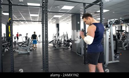 Strong man with injured elbow training with dumbbell in gym, recovery, strength Stock Photo