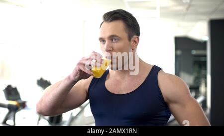 Bodybuilder drinking fresh orange juice, balanced fitness nutrition, workout Stock Photo