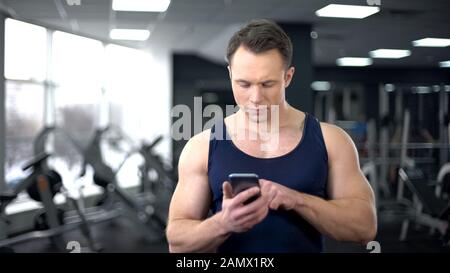 Sportsman checking fitness application in smartphone, personal program online Stock Photo