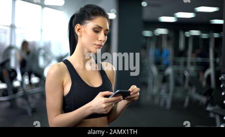Fit woman checking workout results at smartphone in gym, sport innovation Stock Photo