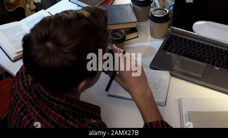 Schoolboy drinking coffee while preparing for exam at night, doing homework Stock Photo