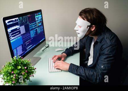 Anonymous computer hacker in white mask and hoodie. Obscured dark face making silence gesture in Underground Secret Location Surrounded by Displays an Stock Photo