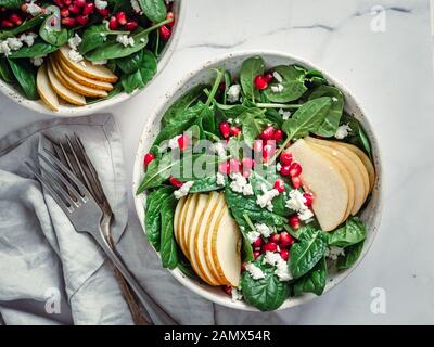 Fresh salad with baby spinach, pear, pomegranate and cottage cheese. Two bowls with delicious summer fruit salad on marble table. Copy space for text. Ideas and recipes for healthy breakfast or lunch Stock Photo