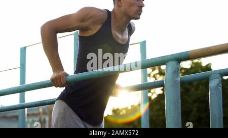 Muscular young male doing exercises on parallel crossbars outdoors, sport Stock Photo