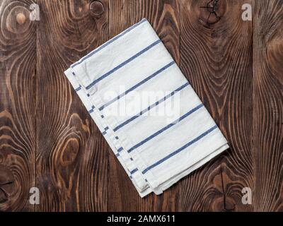 View from above on brown wooden table with linen kitchen towel or textile napkin. Blue folded tablecloth on dark brown wood tabletop. Copy space for text. Can use as mock up for design Stock Photo