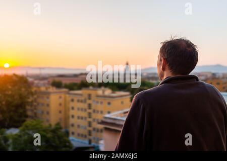 Back of young man watching sunset in Rome, Italy city with church tower in summer evening sunset night cityscape skyline mountain aerial view Stock Photo