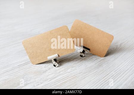 Two blank kraft business cards and metal binder clips on light wood table background. Stock Photo