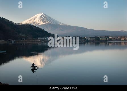 View of Mount Fuji reflected in the lake Kawaguchiko with fishermen out fishing on the lake Stock Photo