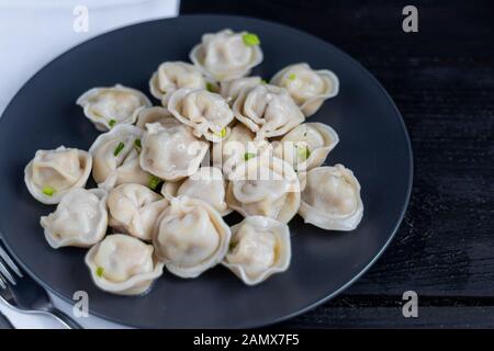 Boiled dumplings decorated with onions and peppers. In the background are greens, red peppers and bay leaves. On a black wooden background with a whit Stock Photo