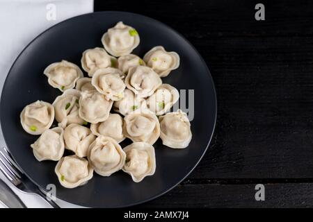 Boiled dumplings decorated with onions and peppers. In the background are greens, red peppers and bay leaves. On a black wooden background with a whit Stock Photo