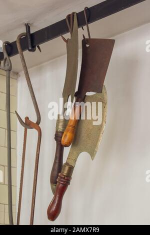 Old butchers cleavers and tools hanging from hooks. Stock Photo