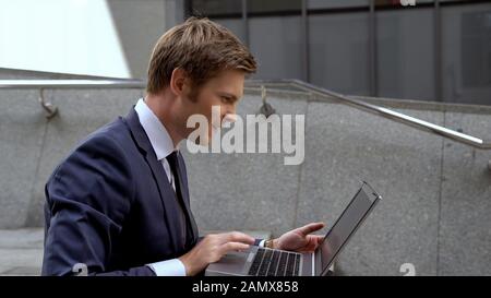 Businessman checking stock market using laptop on stairs outdoors office center Stock Photo