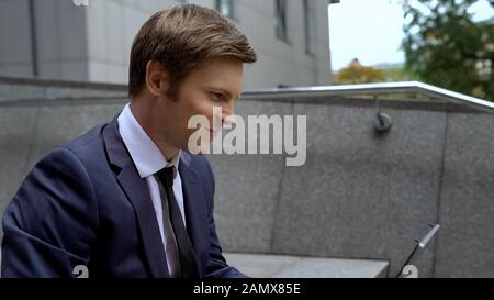 Delighted male in business suit working on laptop on stairs outdoors, ambitions Stock Photo