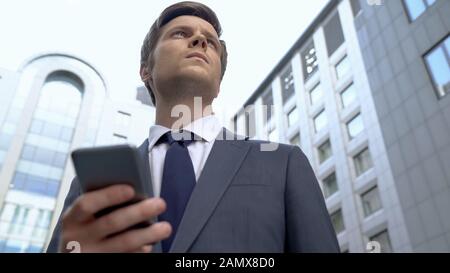 Young pensive broker reading news on smartphone, receiving latest information Stock Photo
