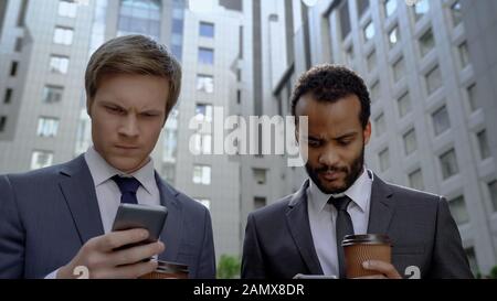 Pensive businessmen checking stock market news using apps for phones, gadget Stock Photo