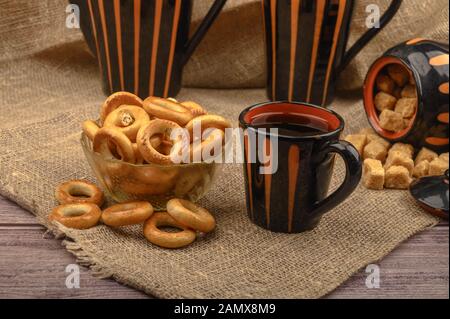 Small bagels, brown sugar, a mug of tea and ceramic dishes on a background of rough homespun fabric close-up Stock Photo