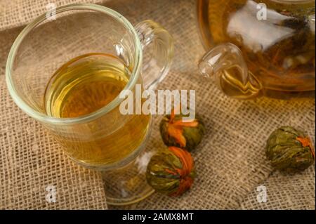Flower tea brewed in a glass teapot, a glass of tea and balls of flower tea on a background of rough homespun fabric. Close up Stock Photo