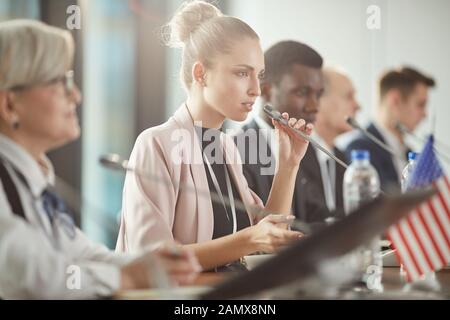 Young female political leader speaking the speech into the microphone at business conference Stock Photo