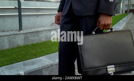 Manager holding eyeglasses and leather briefcase, tired after long working day Stock Photo