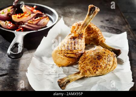 Grilled spiced chicken drumsticks with an accompaniment of roast vegetables in a skillet served on crumpled white paper Stock Photo
