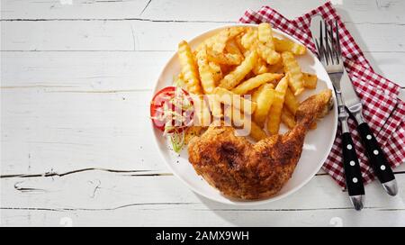 Barbecued marinated spicy seasoned chicken leg with crinkle cut potato chips, pommes frites or French fries on a plate with napkin and utensils from a Stock Photo