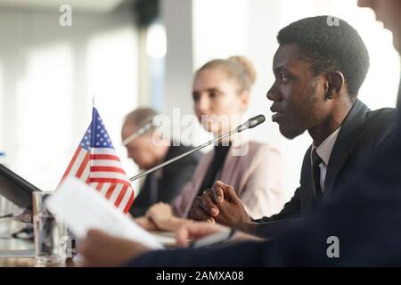 Side view of African businessman performing during conference he sitting at the table and speaking into the microphone Stock Photo