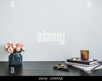 Home office desk with copy space. Pink flowers, scented candle, stack of books on black tabetop. Copy space for text. Home office desk workspace. Empty white room with wooden table Stock Photo