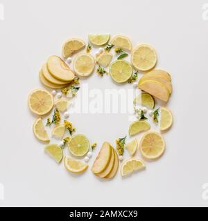 Creative pattern of sliced fruits and yellow blooms. Green apple, green and yellow lemons arranged in a circle. Flat lay with copy space Stock Photo