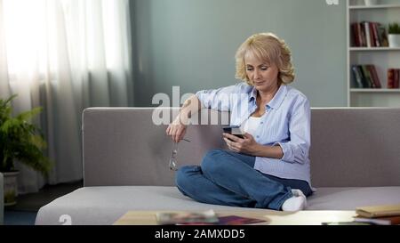 Nice middle-aged woman sitting on couch with smartphone, gadget application Stock Photo