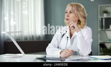 Thoughtful female doctor sitting at table, analysing patient results, diagnosis Stock Photo