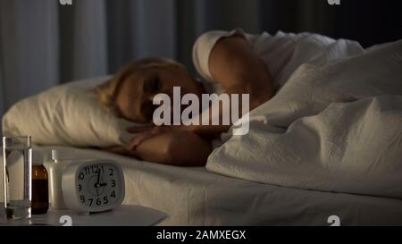 Middle-aged sick lady sleeping with pills and water glass on table, health Stock Photo