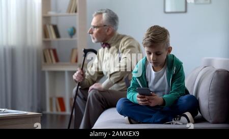 Boy using mobile phone, upset granddad sitting aside, internet addiction concept Stock Photo