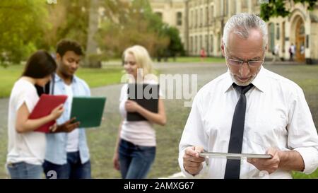 Senior male dean scrolling mobile app on tablet, technology in education Stock Photo