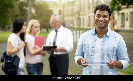 Cheerful mixed-race male holding tablet, using mobile application for education Stock Photo