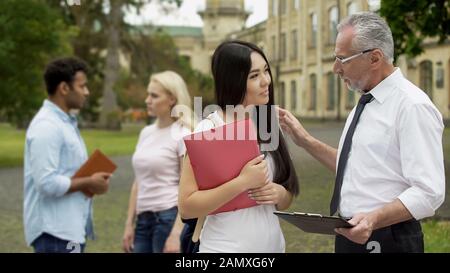 Senior professor talking to Asian student, discussing science project on campus Stock Photo
