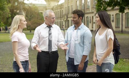 Senior geography teacher talking with students near college, explaining topic Stock Photo
