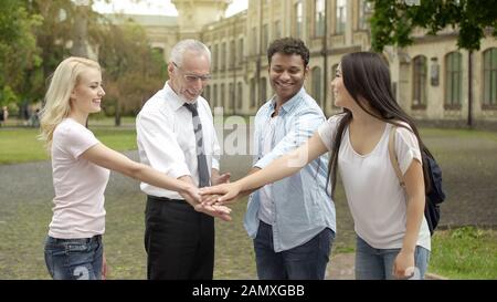 Happy teacher and multiracial students putting hands on pile, team building Stock Photo