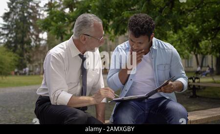 Teacher and smart Hispanic student discussing science project near university Stock Photo